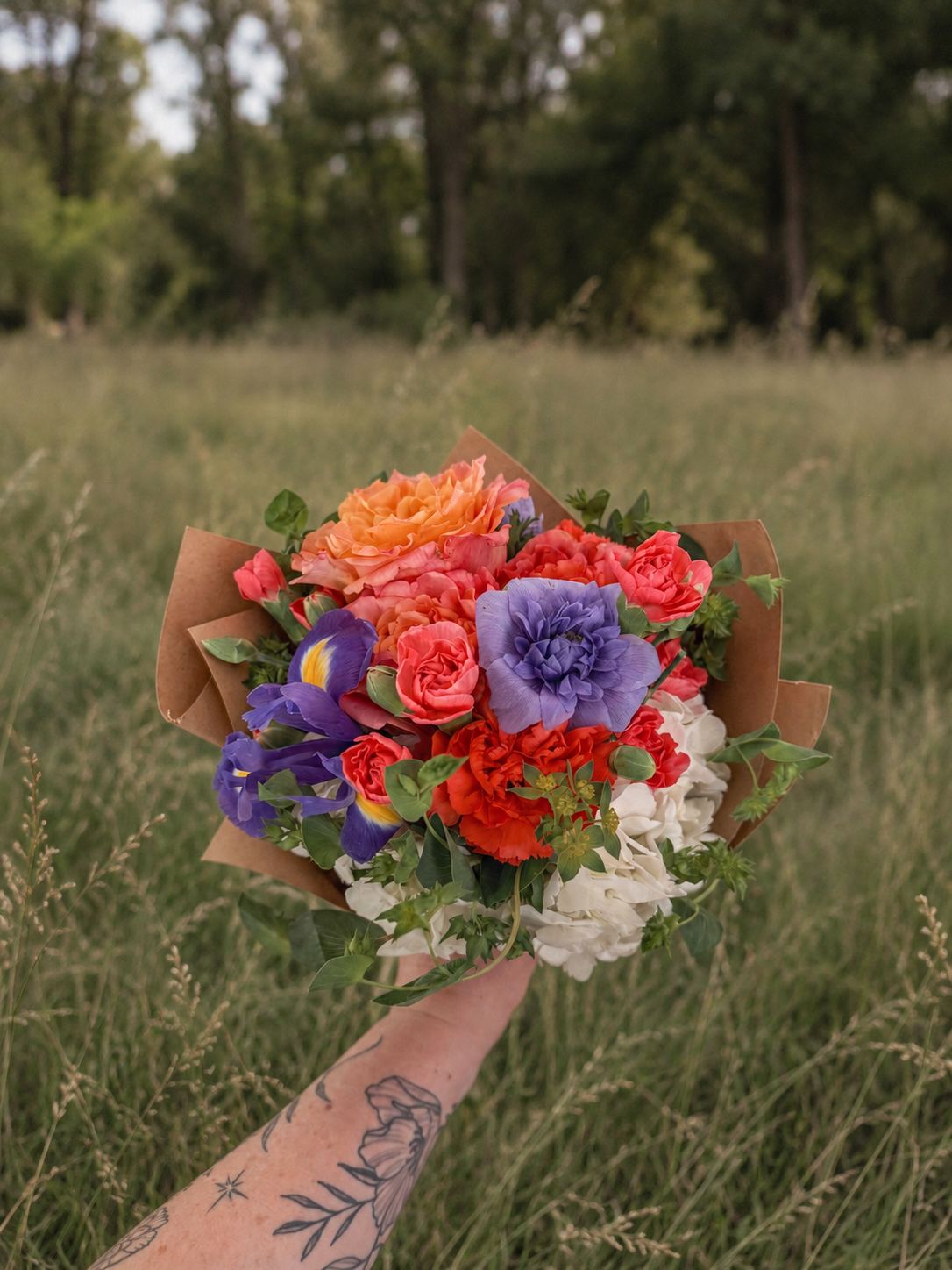 A bouquet of orange roses, purple anemones and red blooms held in tall grass