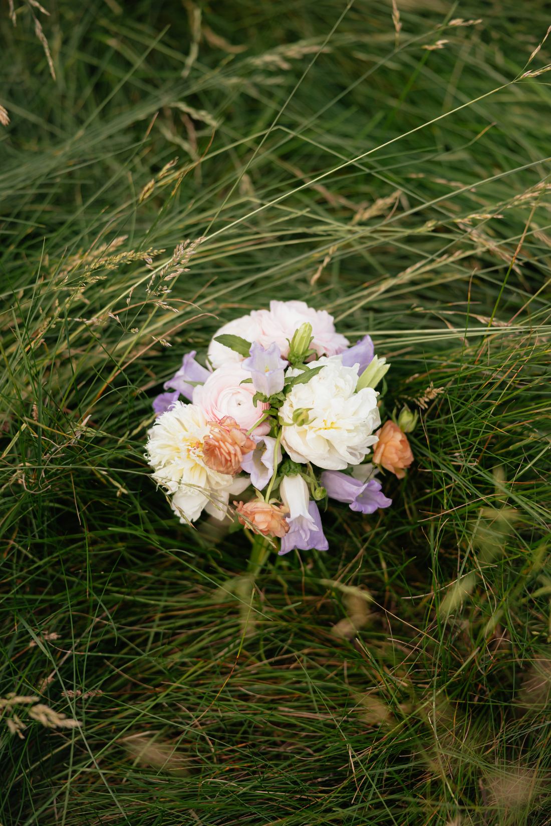 A blush and cream bouquet laid down in tall meadow grass