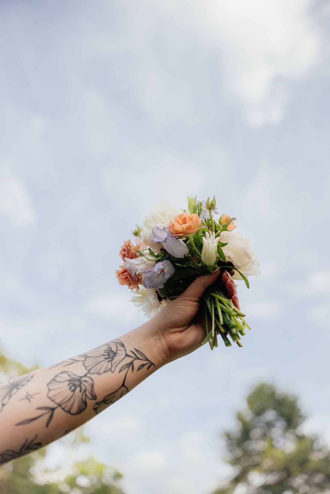 A hand-tied bouquet of garden blooms held up against a blue sky