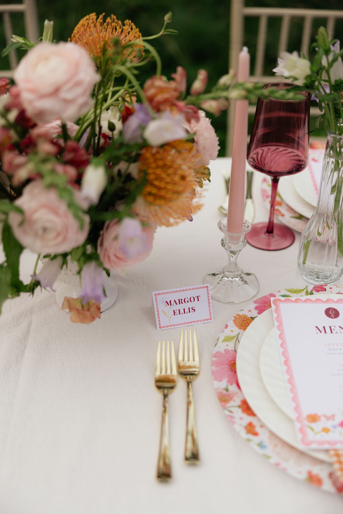 A blush and coral garden centerpiece beside pink glassware on a white table