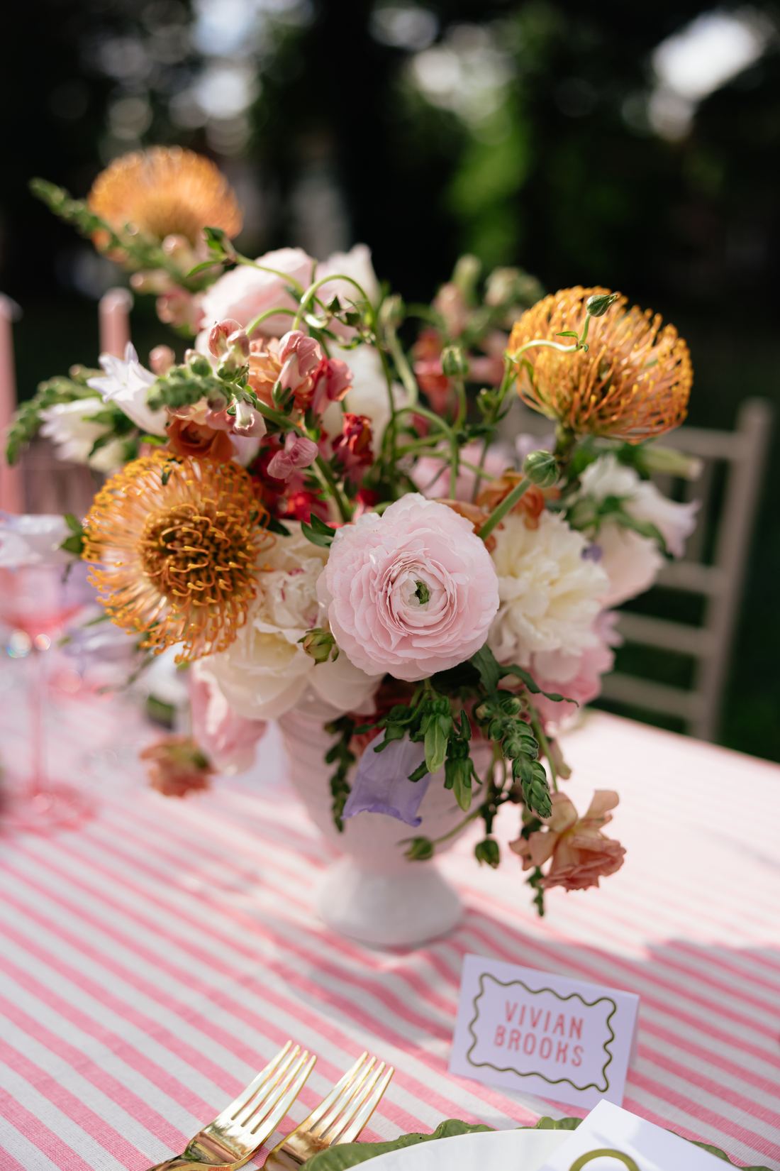 A peach and cream garden arrangement with pincushion protea in a footed vase