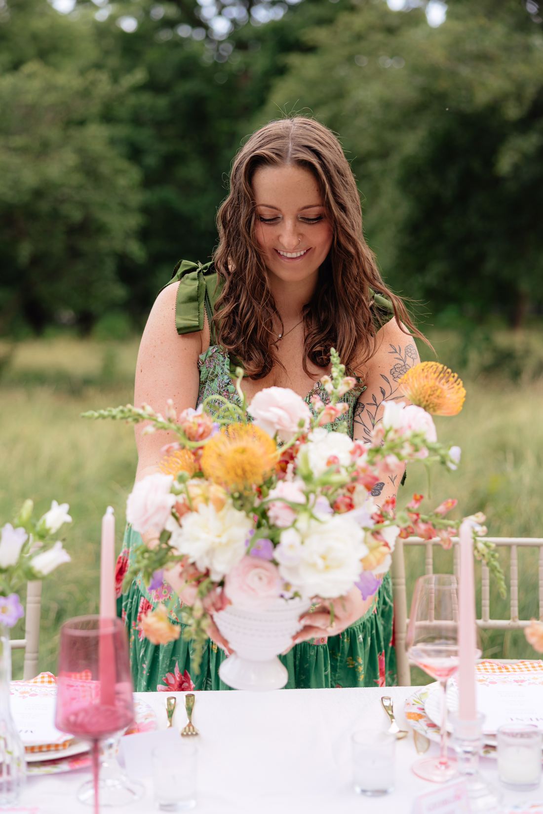 Riley Hogan arranging peach and cream blooms at a styled table in a meadow