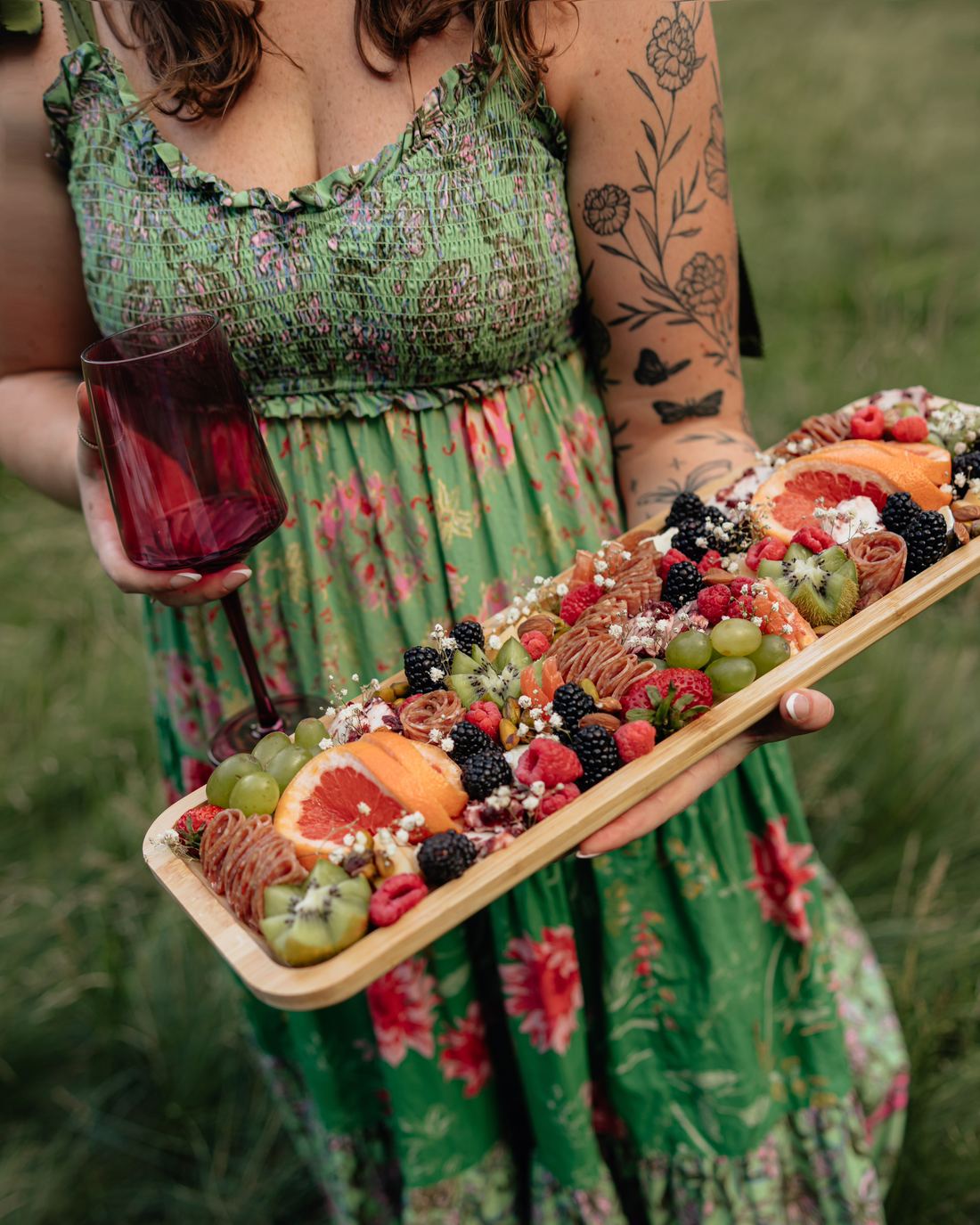 Riley Hogan holding a long grazing board, in a green floral dress