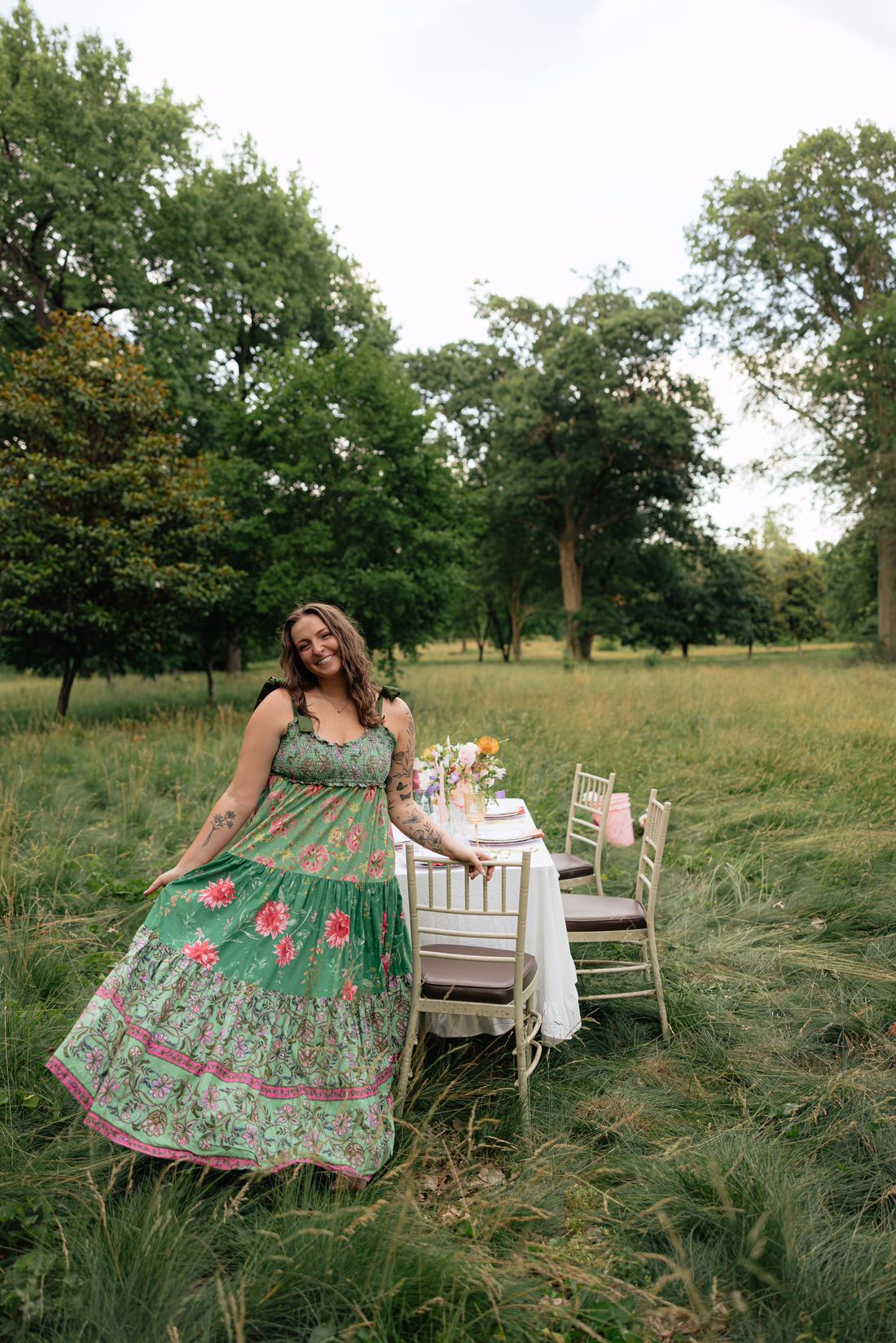 Riley Hogan walking toward a styled table in a meadow, in a green floral dress