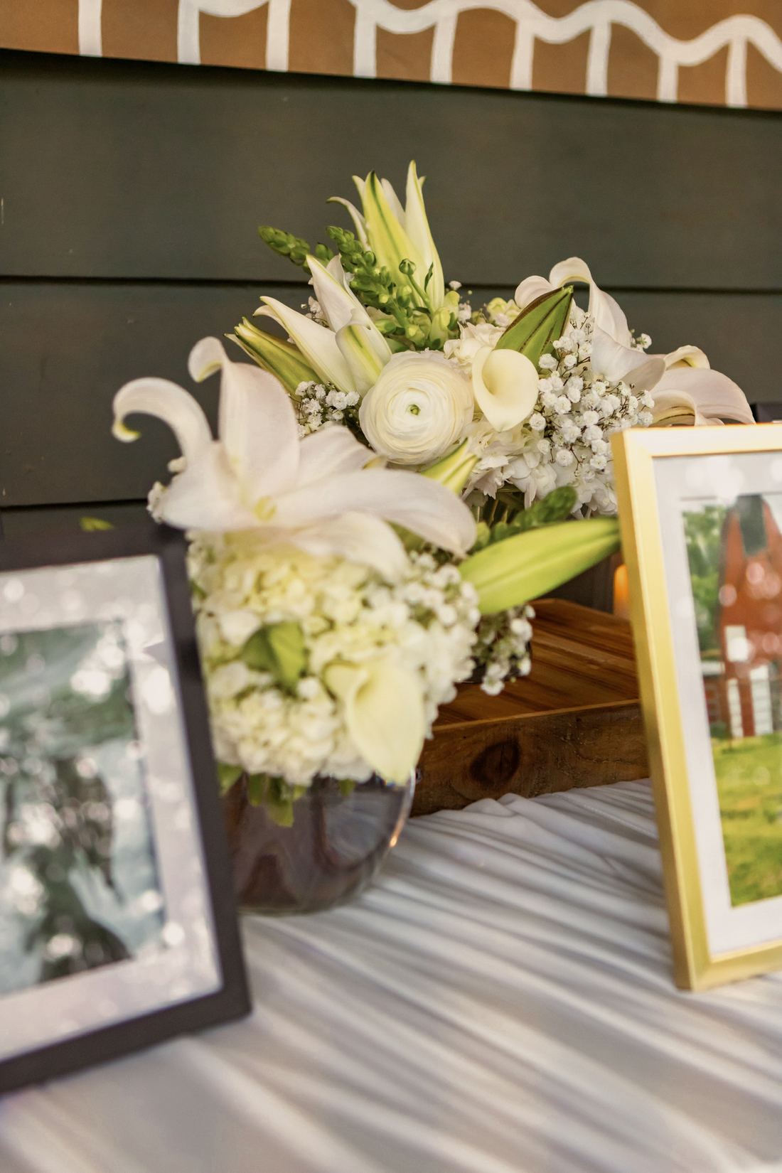 A white arrangement of lilies, calla lilies, ranunculus, hydrangea and baby’s breath in a glass bowl