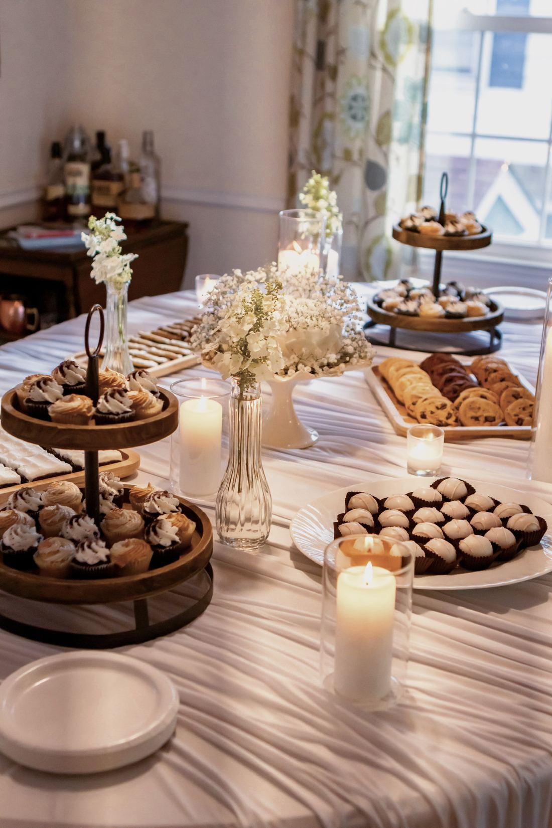 A long dessert table with tiered cupcake trays, cookies, truffles and a white cake