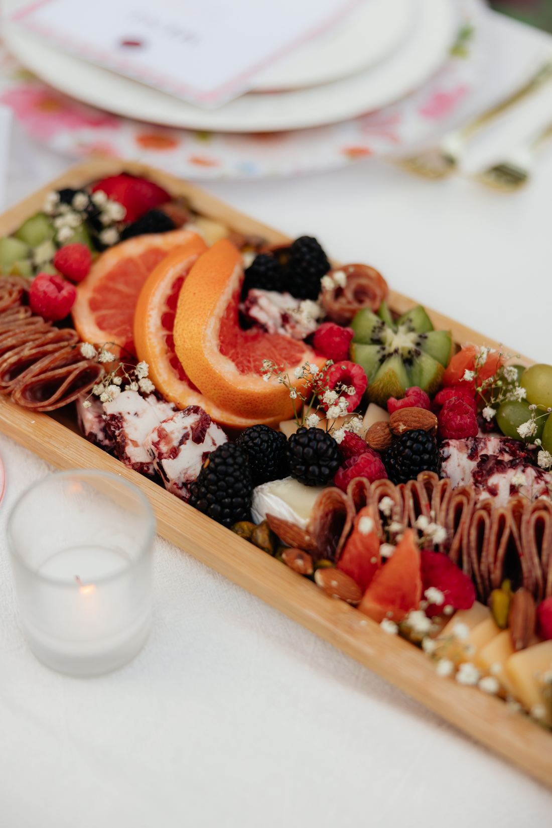 A long wooden grazing board with melon, berries, chocolate-dipped fruit and cheese