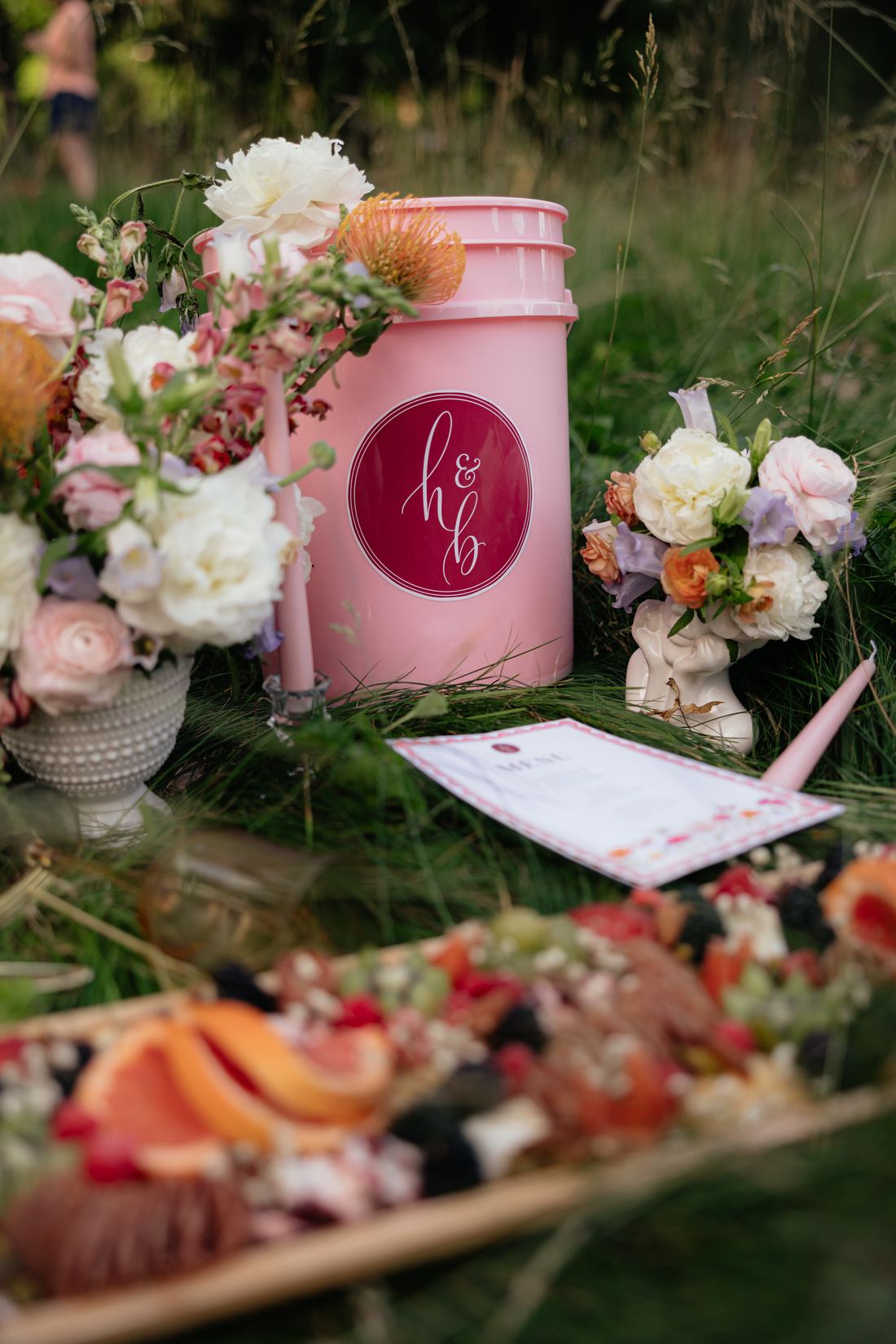 A grazing board on the grass surrounded by florals, a pink tub and a printed menu
