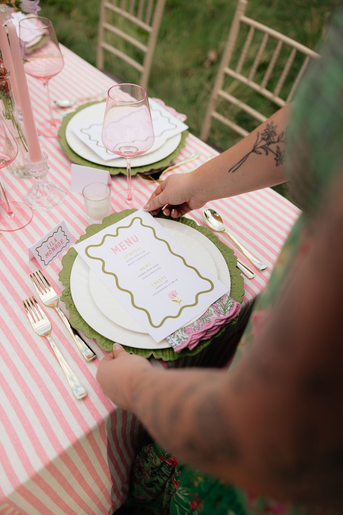 Hands lowering a green scalloped charger onto pink stripe linen