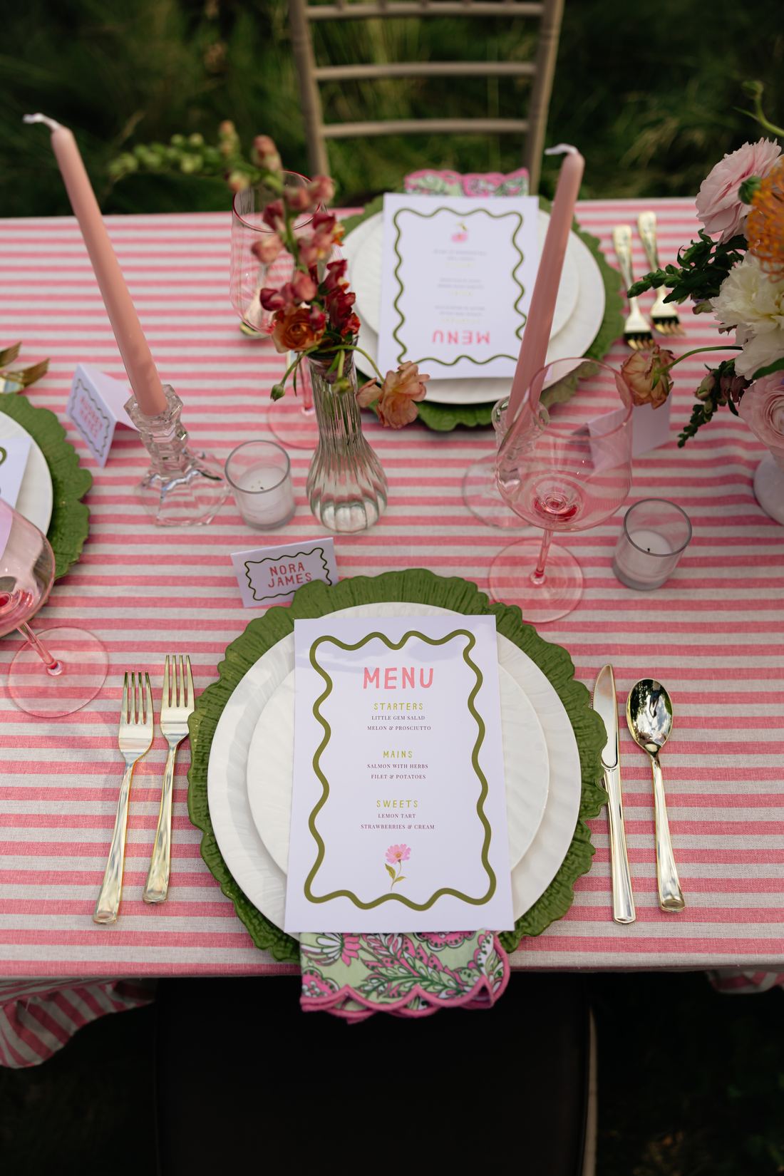 A pink stripe table with scalloped menus, taper candles and garden florals