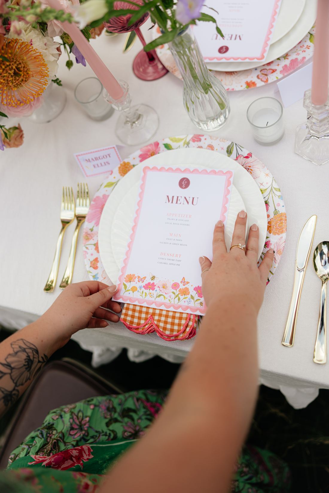 A scalloped-edge menu card resting on a floral charger beside gold flatware