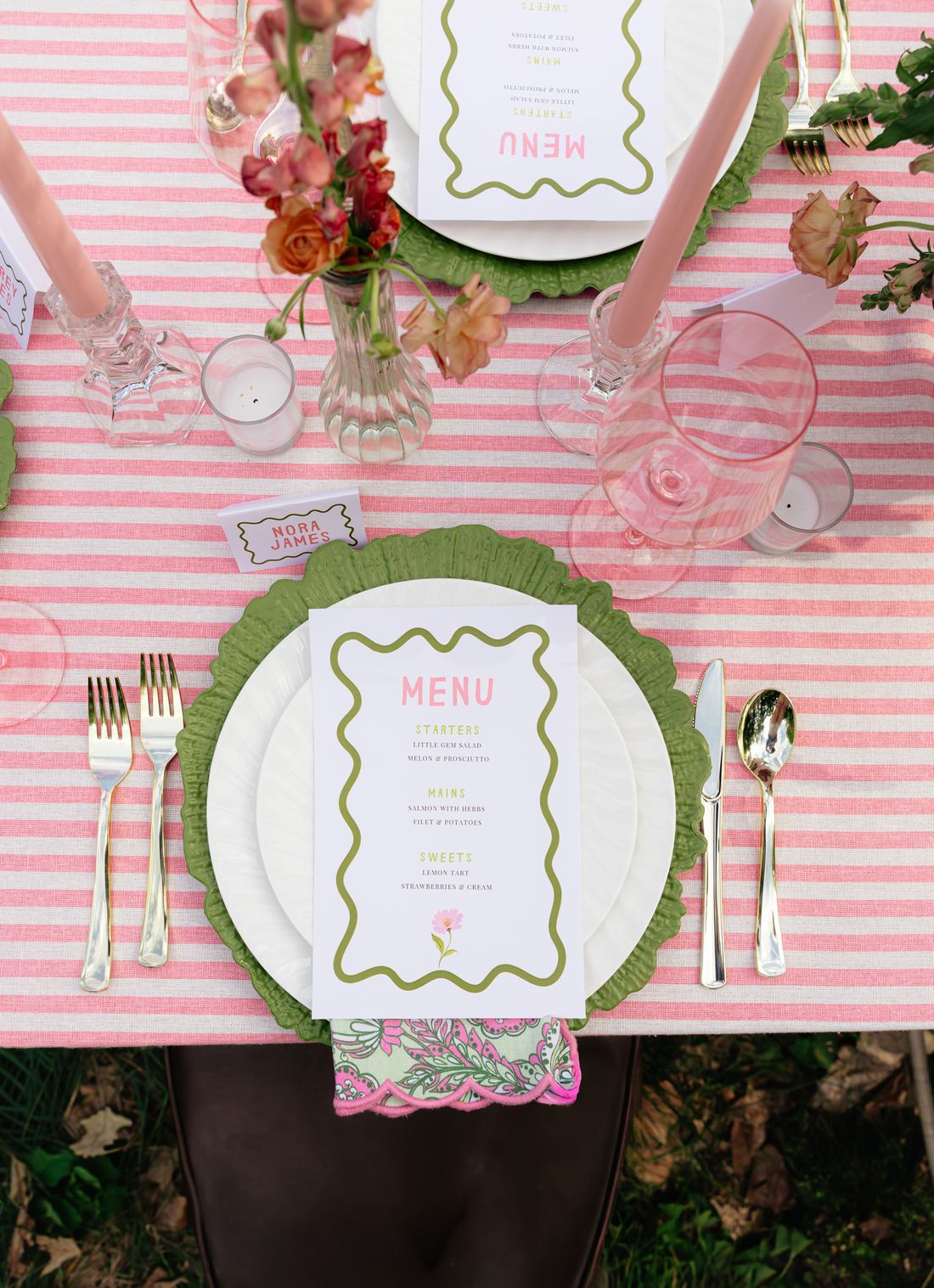 An overhead place setting on pink stripe linen with a green scalloped charger and printed menu