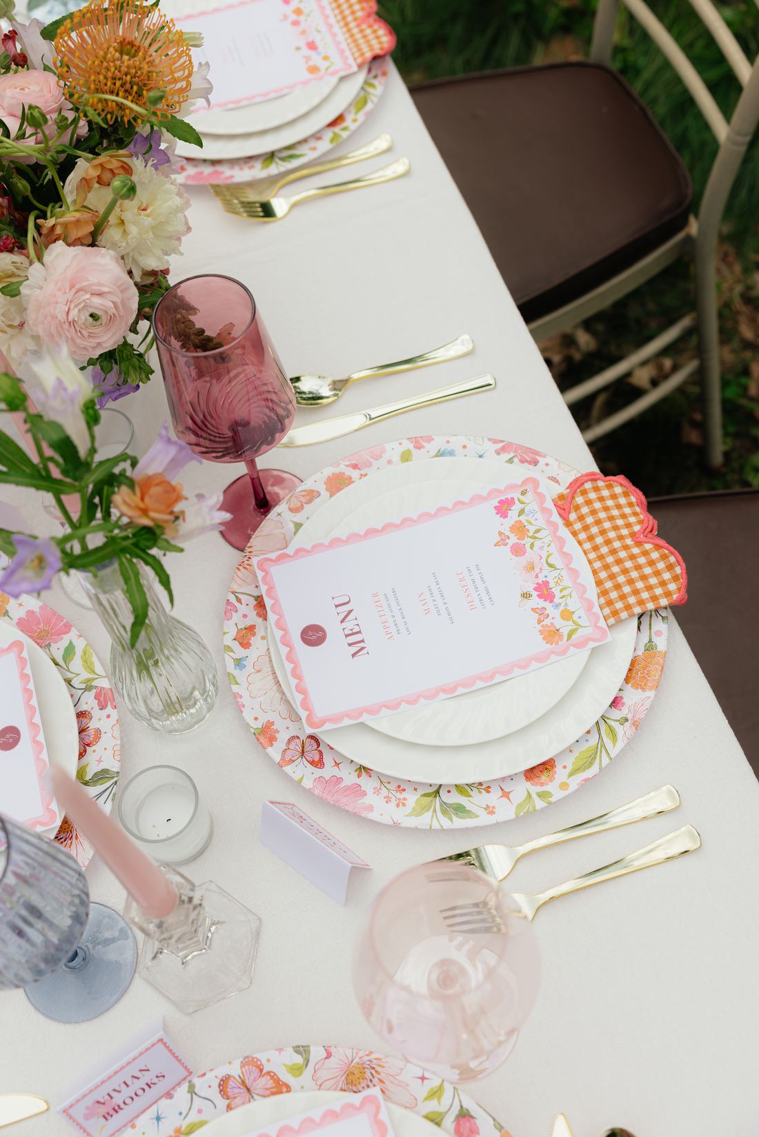 An overhead view of a styled table with bud vases, colored glassware and printed menus