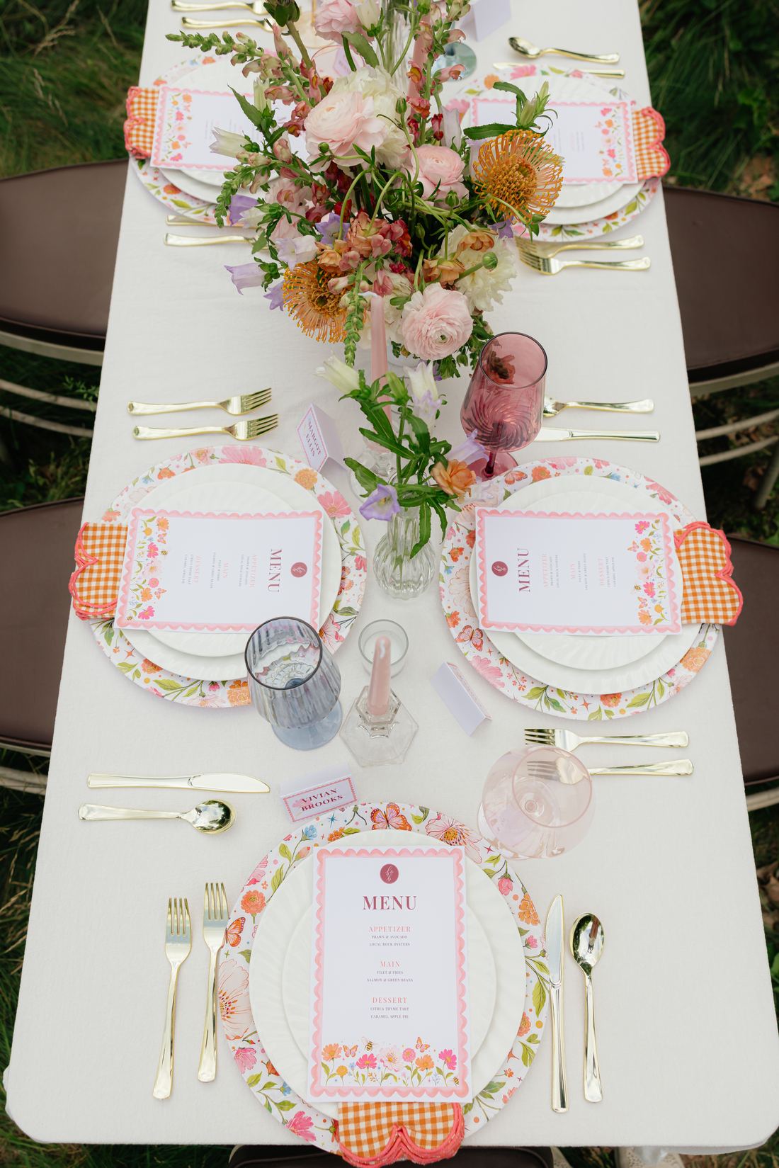 An overhead view of a long white table with coral florals, printed menus and gold flatware