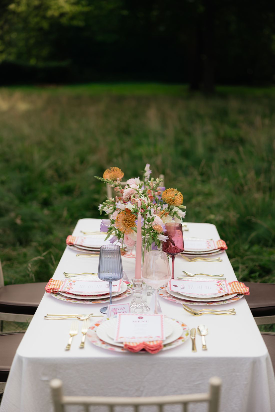 A white table set end to end with peach centerpieces, printed menus and gold flatware