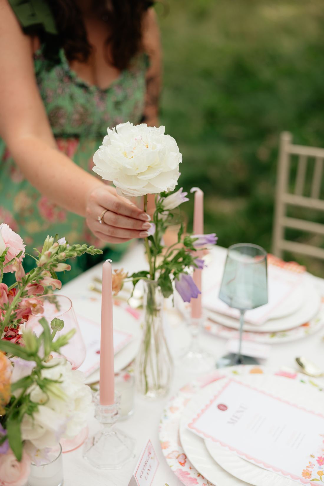 Riley Hogan placing a white peony into a bud vase on a table set with pink taper candles and scalloped menus