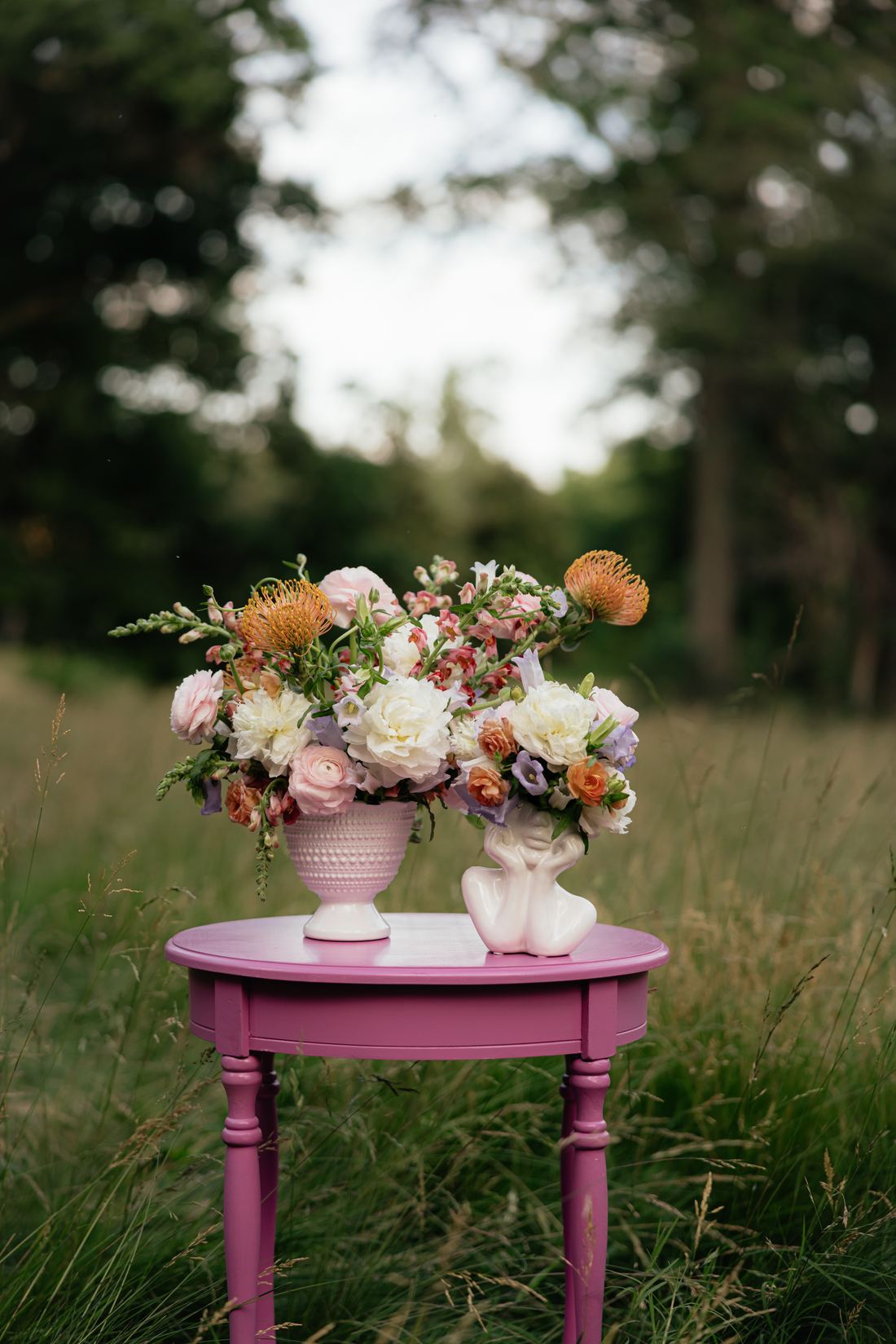 A blush and cream arrangement on a pink side table in a summer meadow