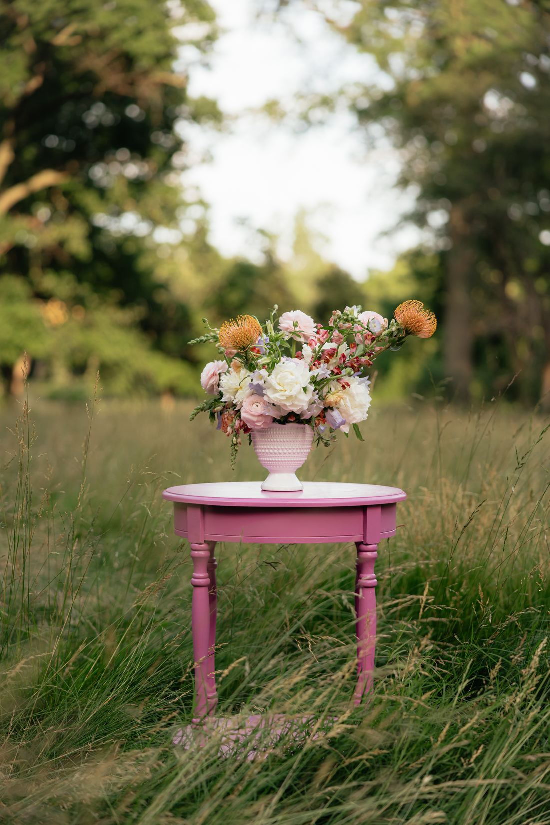 A blush and peach arrangement on a pink side table in a wide summer meadow