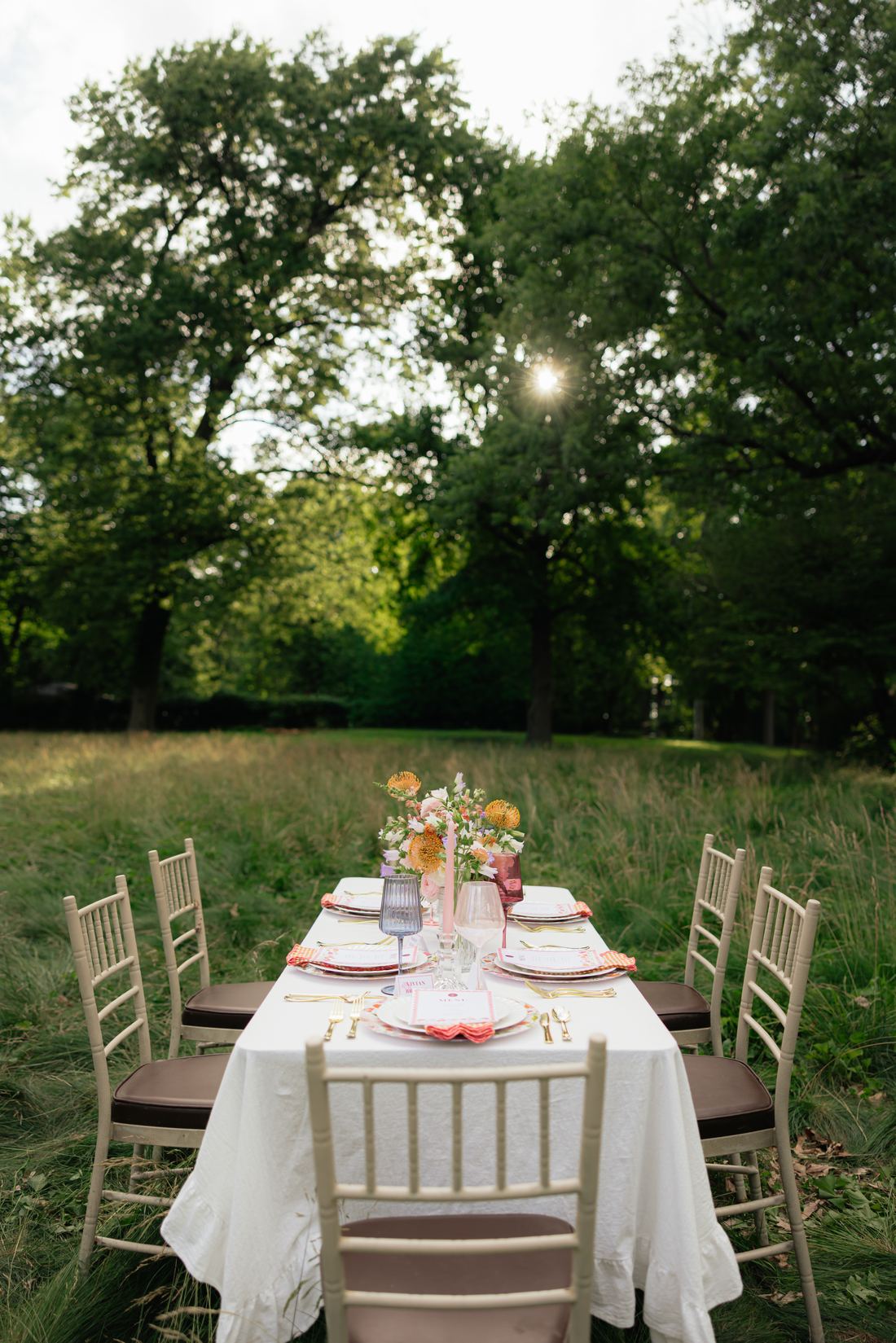 A white table and gold chiavari chairs set for dinner in a meadow at golden hour
