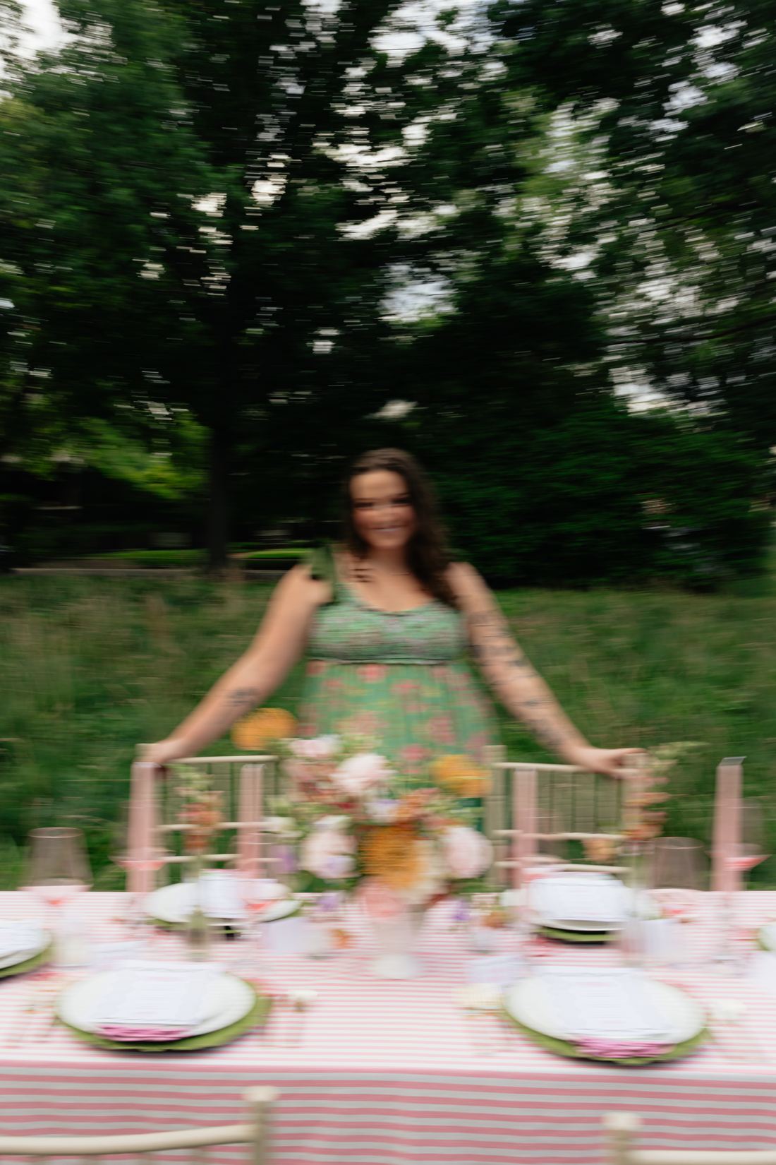 Riley Hogan finishing a long pink stripe table with gold chairs in a meadow