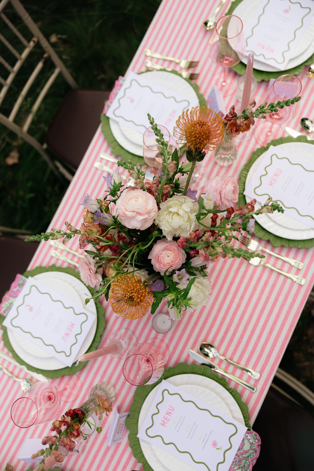 A pink stripe runner down a white table with green chargers and a garden centerpiece