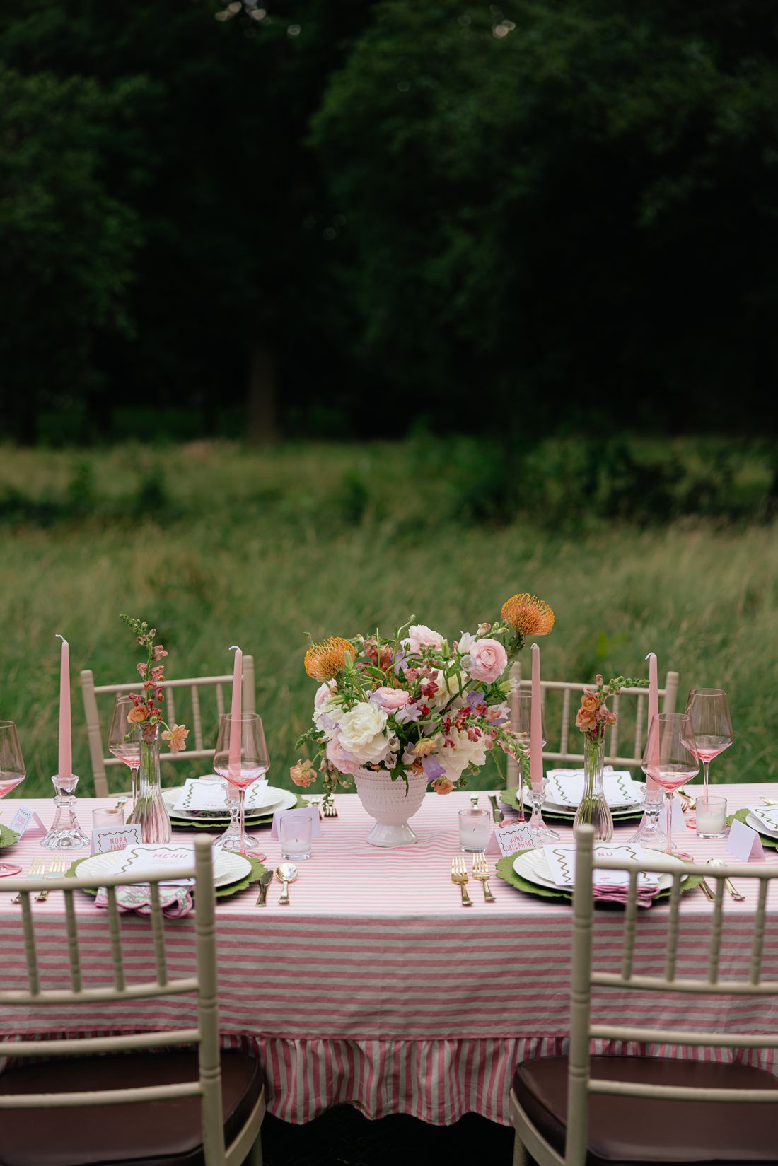 A fringed pink stripe table with gold chairs and coral florals photographed at dusk