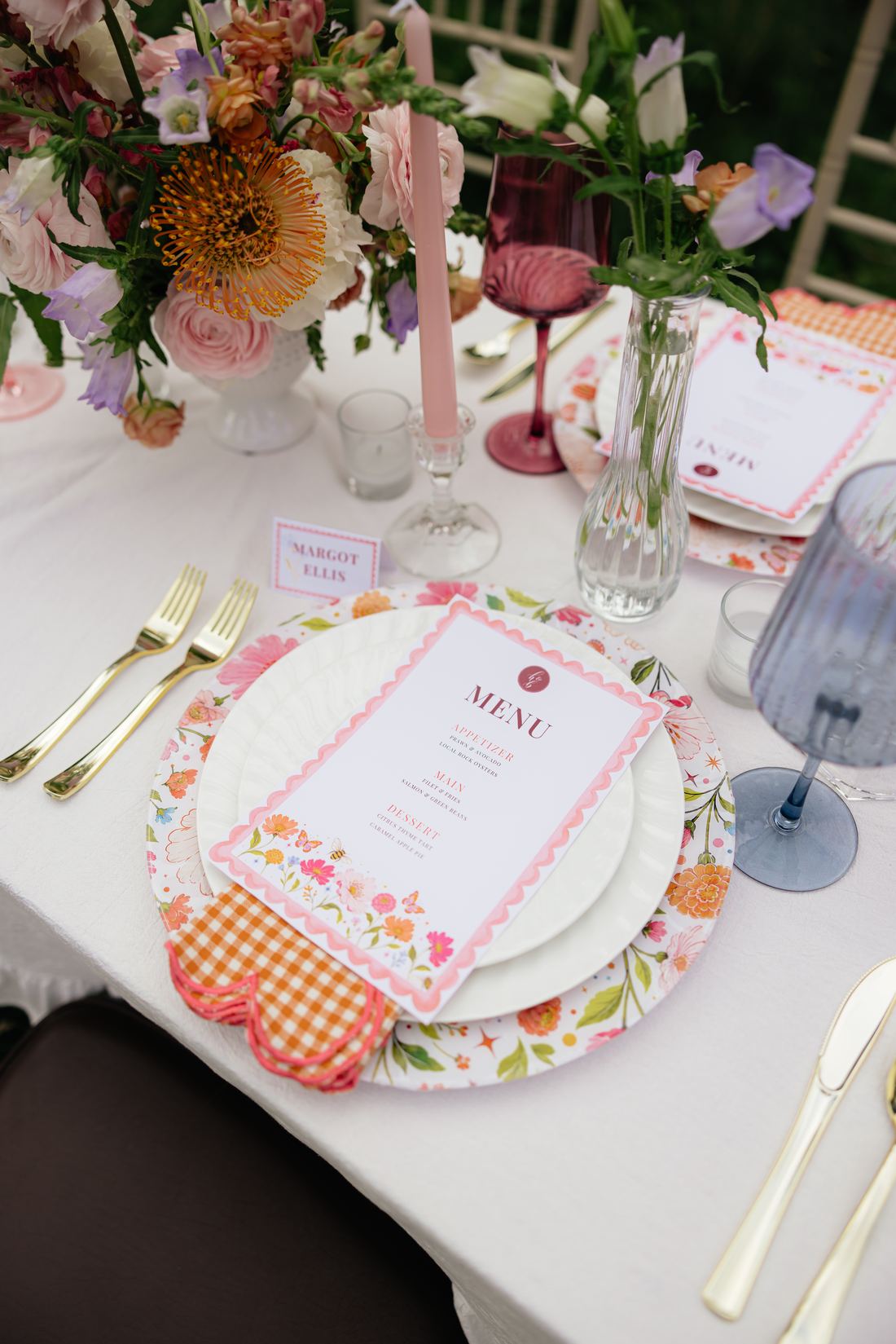 Colored glassware, gold flatware and a floral-printed charger seen close up
