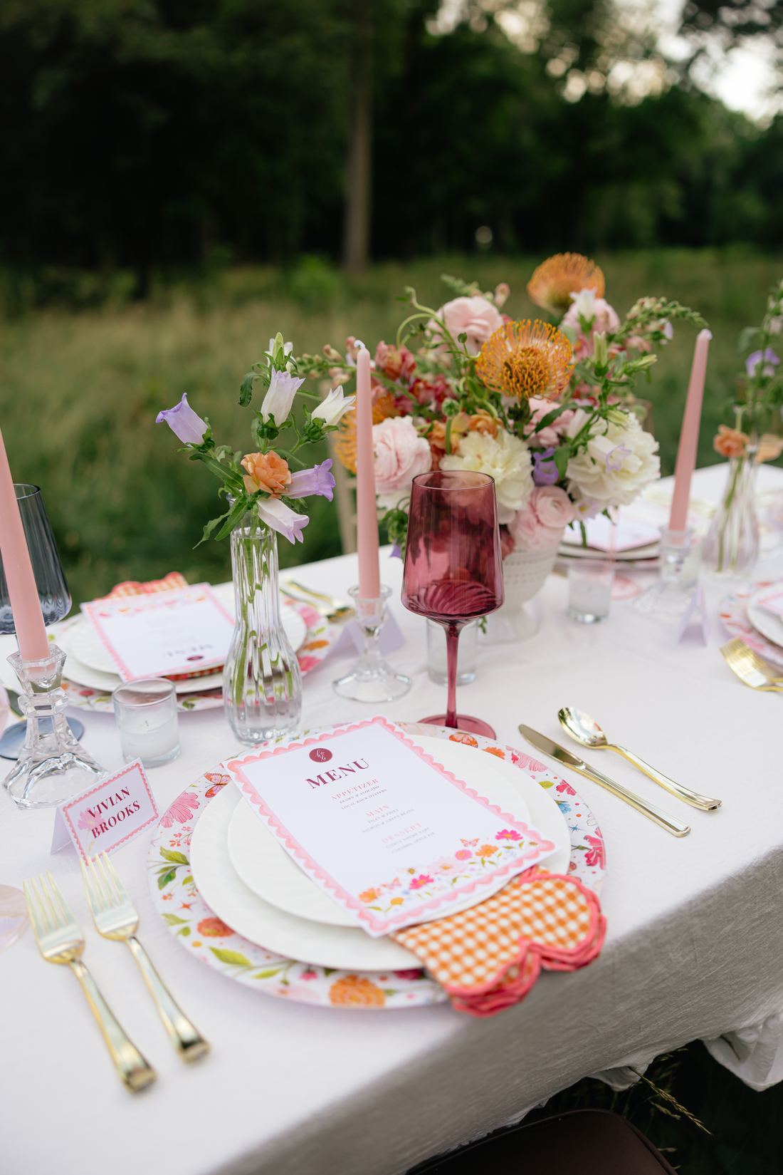 A white table with gold flatware, a floral charger, bud vases and coral blooms