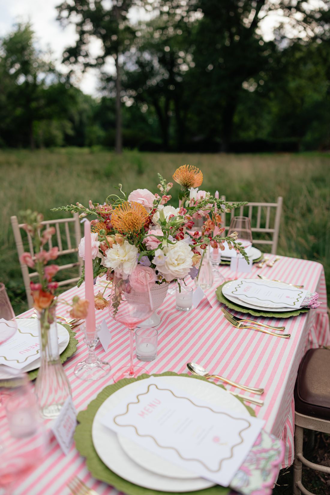 A pink stripe table with green scalloped chargers, gold flatware and a garden centerpiece