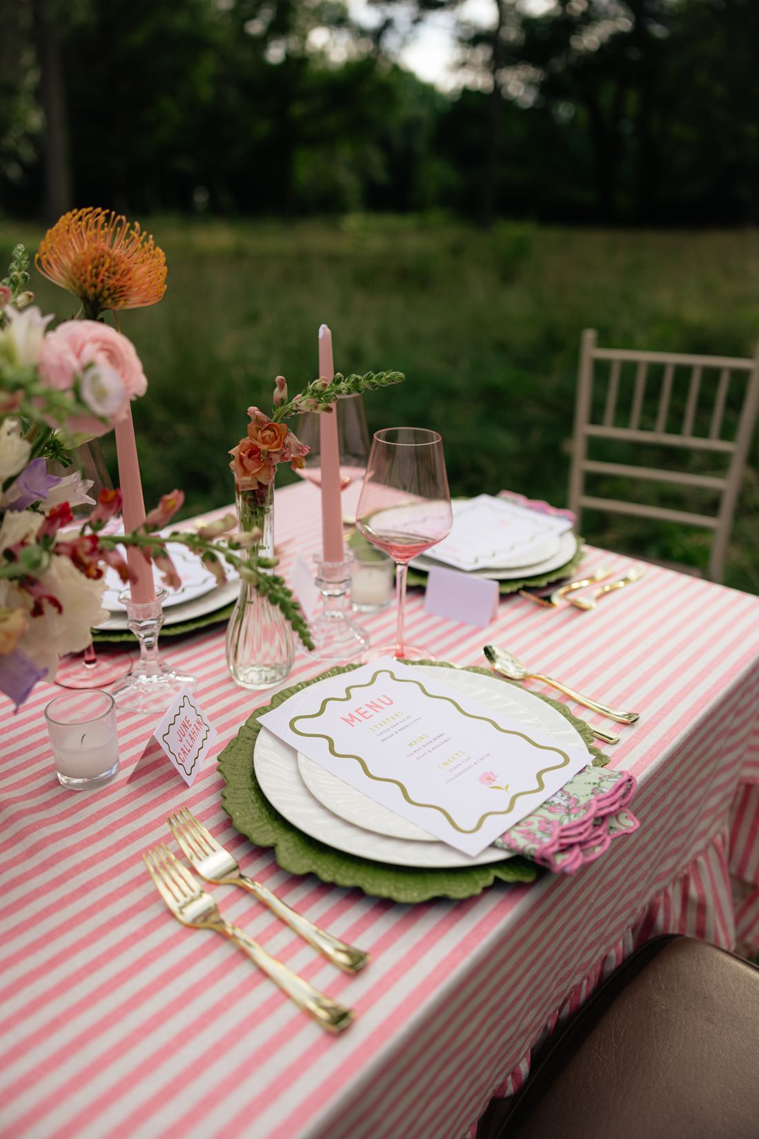 Pink stripe linen laid with a scalloped charger, gold flatware, pink glassware and taper candles