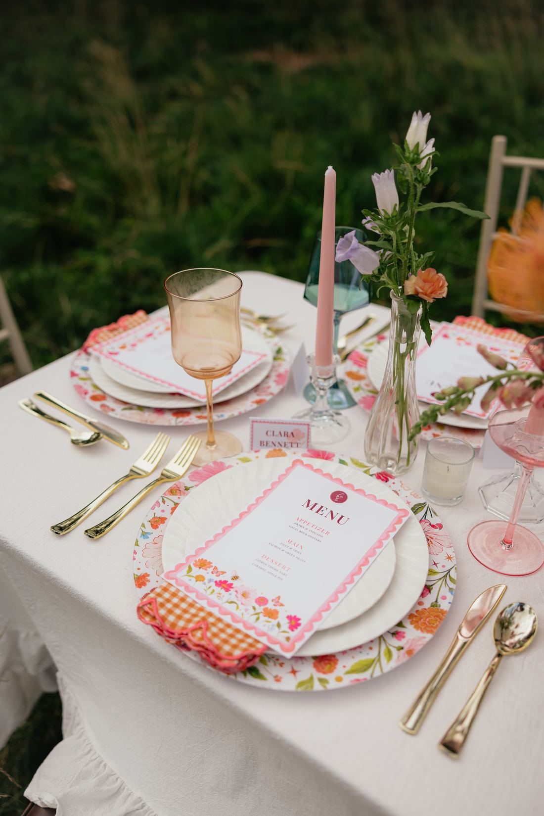 A white table with pink taper candles, bud vases, a floral charger and a menu card